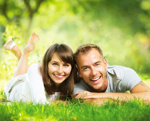 Couple laying in the grass smiling with gorgeous smiles from cosmetic dentistry services like the ones offered by Lisa Siddall DDS.